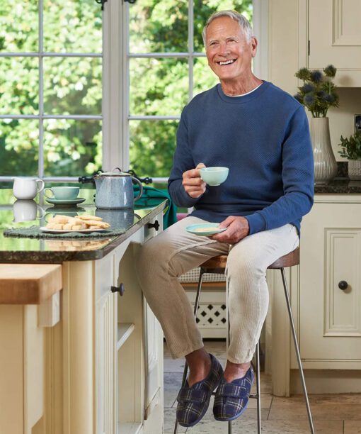 Man sitting at breakfast bar drinking coffee wearing Cosyfeet Ronnie mens slipper in Navy Highland