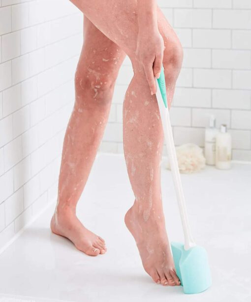 A lady in the shower using a long handled toe sponge to wash her feet